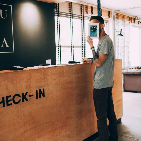 Guest checks in at a wooden front desk labeled 'CHECK-IN' in a modern lobby, holding a blue card in front of their face.
