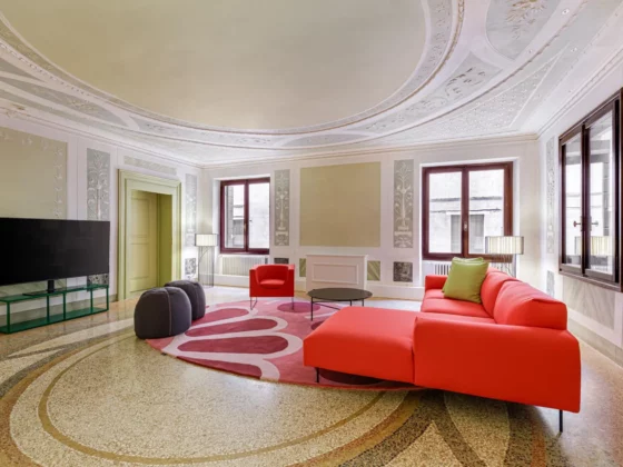 Elegant living room with ornate ceiling, pastel walls, and a bright red sectional sofa around a pink circular rug.