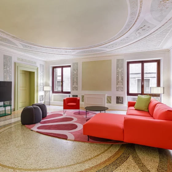 Elegant living room with ornate ceiling, pastel walls, and a bright red sectional sofa around a pink circular rug.