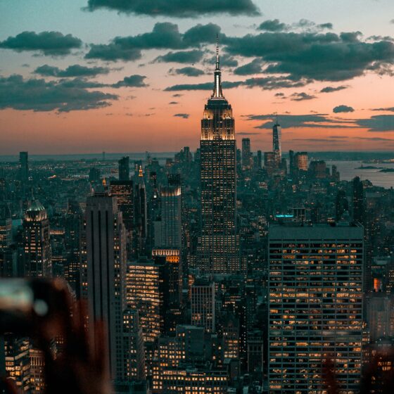 New York City skyline at sunset with the Empire State Building lit up against a pink-orange sky.