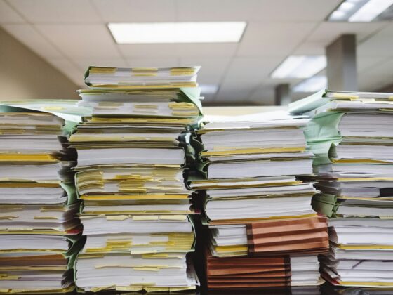 Stacks of file folders and documents piled high on desks in an office setting