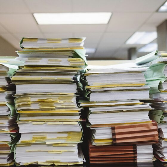 Stacks of file folders and documents piled high on desks in an office setting