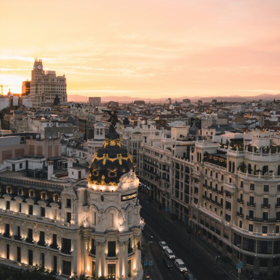 Madrid's Metropolis Building at sunset, ornate white facade and gold dome above a bustling city street.