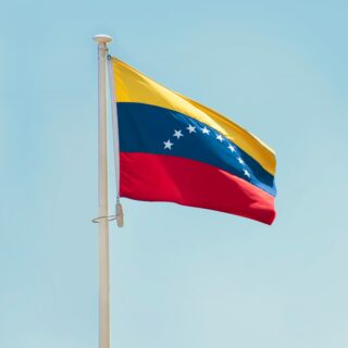 Venezuela flag waving on a flagpole against a bright blue sky outside.
