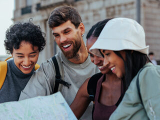 Four friends smiling while looking at a folded map in an urban street. (informative)