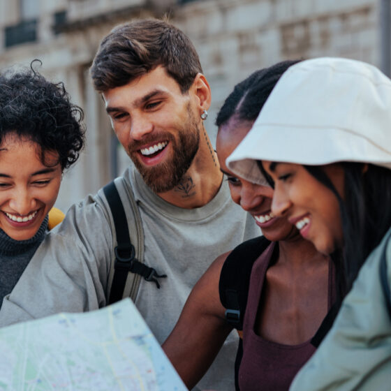 Four friends smiling while looking at a folded map in an urban street. (informative)