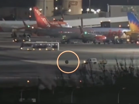 Nighttime at the airport with aircraft parked; a small dark object on the taxiway circled in orange.