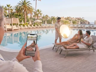Photographer captures a couple lounging by a pool while using a reflective round light nearby, with a guest taking a photo in the foreground.