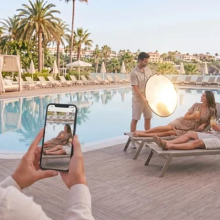Photographer captures a couple lounging by a pool while using a reflective round light nearby, with a guest taking a photo in the foreground.