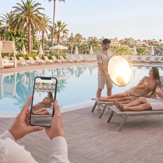 Photographer captures a couple lounging by a pool while using a reflective round light nearby, with a guest taking a photo in the foreground.