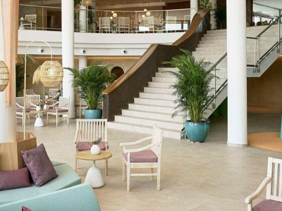 Indoor hotel lobby-style lounge with pastel seating, purple cushions, wicker pendant lights, and a bright teal spiral slide near the stairs.