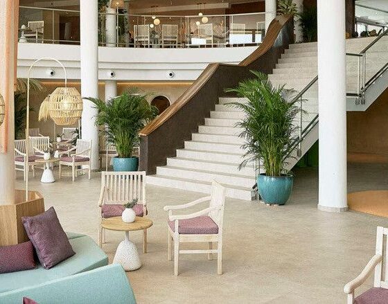 Indoor hotel lobby-style lounge with pastel seating, purple cushions, wicker pendant lights, and a bright teal spiral slide near the stairs.