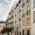Row of light-colored apartment buildings with decorative balconies lining a narrow street.