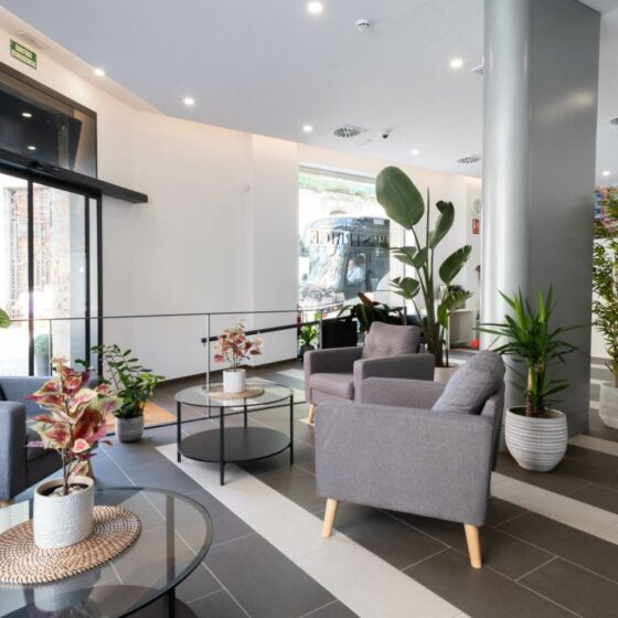 Modern lobby with gray armchairs, glass coffee tables, and potted plants near large glass doors: bright and welcoming space.