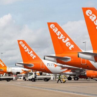 Multiple bright orange easyJet airplanes are parked at a busy tarmac with ground support vehicles nearby.