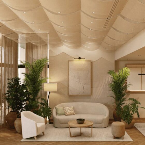 Open, sunlit living room with beige curved sofa, round coffee table, and tall potted plants in a neutral, modern space.