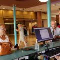 Hotel front desk staff assisting a female guest with a large brown handbag at the lobby counter.
