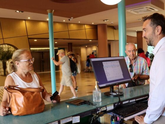 Hotel front desk staff assisting a female guest with a large brown handbag at the lobby counter.