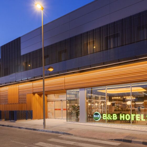 Modern hotel exterior at dusk with glass storefront and a bright green B&B HOTELS sign