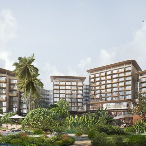 A modern tropical hotel complex with curved glass buildings, a central pool, and lush landscaping including palm trees and greenery.