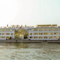 Large white passenger ferry with multiple decks sailing on a calm river at sunset.