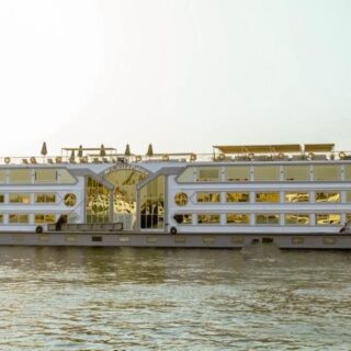 Large white passenger ferry with multiple decks sailing on a calm river at sunset.