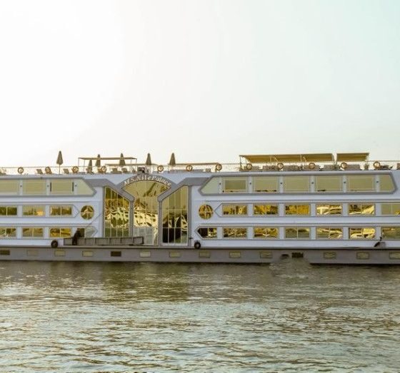 Large white passenger ferry with multiple decks sailing on a calm river at sunset.
