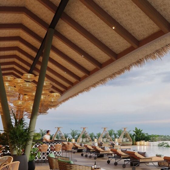 Open-air resort terrace with wicker chairs, circular pendant lights, and an infinity pool overlooking the ocean.