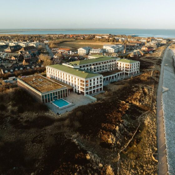 Aerial view of a seaside town with a large modern hotel complex beside a beach and a swimming pool.