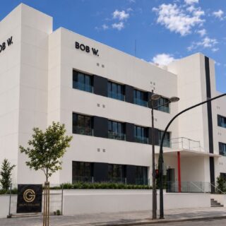 Modern white, multi-story office building with 'BOB W.' signs on the façade, daytime city street view.