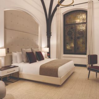 Elegant hotel room with a large bed, tufted headboard, and warm lighting under dark arched beams.” (informative description)