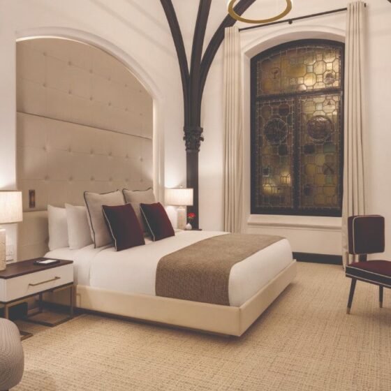 Elegant hotel room with a large bed, tufted headboard, and warm lighting under dark arched beams.” (informative description)