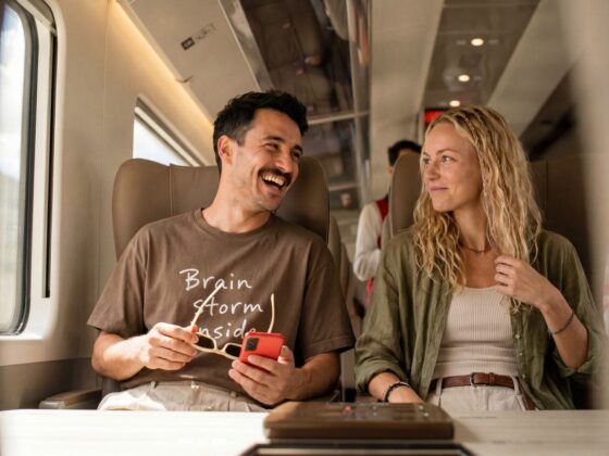 Two friends sitting on a train, smiling and talking with each other.