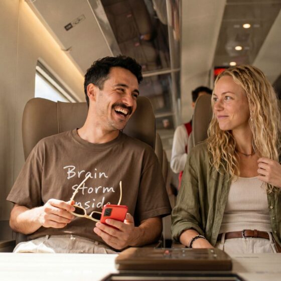 Two friends sitting on a train, smiling and talking with each other.