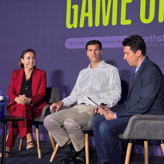 Panelists seated on stage during a conference, purple backdrop with 'GAME ON' signage behind them.