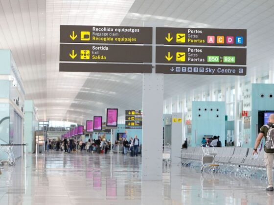 Airport terminal corridor with overhead signs directing to baggage claim, exits, gates, and Sky Centre in multiple languages.