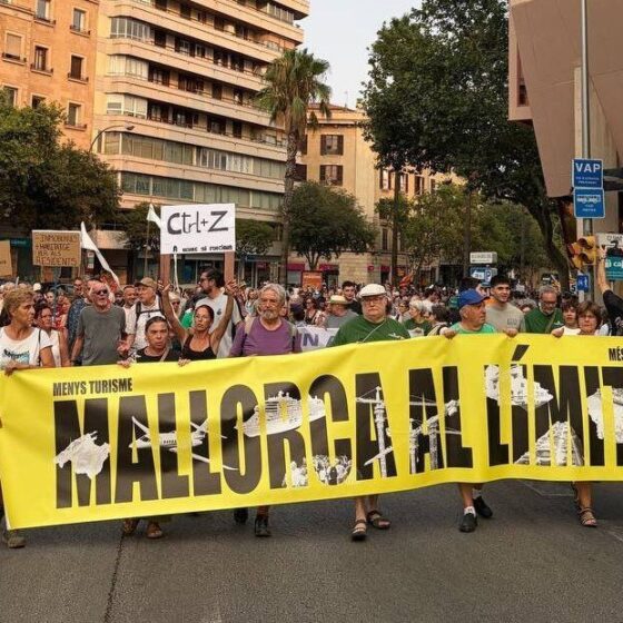 Group of protesters marching down a city street, holding a large yellow banner that reads 'MALLORCA AL LÍMIT' in bold black letters.