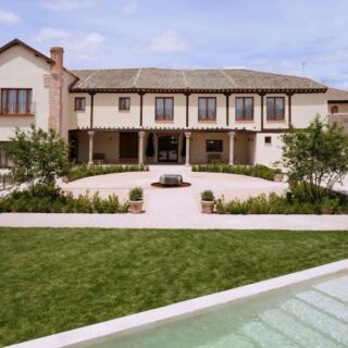 Two-story beige villa with brick accents, central courtyard, and manicured garden paths.”,