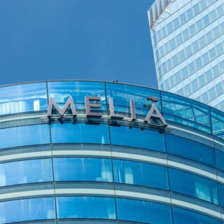 Exterior view of a curved blue glass building with a Melia hotel sign on the facade, under a clear blue sky