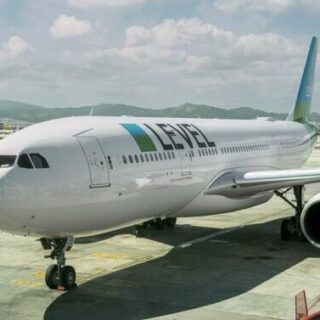 White LEVEL airliner parked at a gate with a jet bridge attached and mountains in the background.
