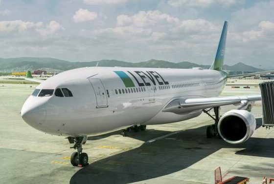 White LEVEL airliner parked at a gate with a jet bridge attached and mountains in the background.