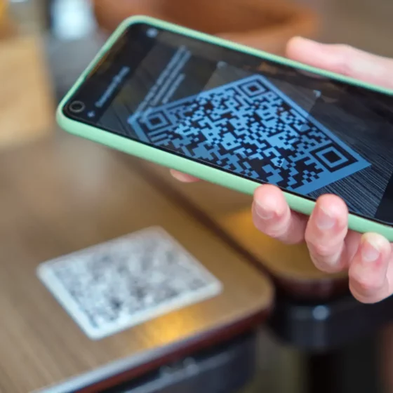 Smartphone in a mint-green case showing a QR code on the screen. Readable QR code ready for scanning in a hand-held device.