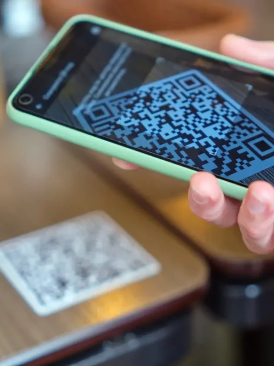 Smartphone in a mint-green case showing a QR code on the screen. Readable QR code ready for scanning in a hand-held device.