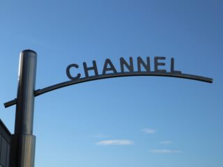 Curved metal sign frame spelling 'CHANNEL' against a clear blue sky, with a tall pole on the left.