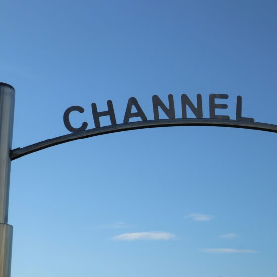 Curved metal sign frame spelling 'CHANNEL' against a clear blue sky, with a tall pole on the left.