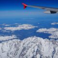 Wing of an Air Berlin aircraft with a red tail fin and logo, flying over snow-covered mountains under a clear blue sky.