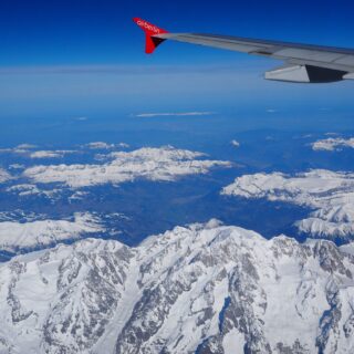 Wing of an Air Berlin aircraft with a red tail fin and logo, flying over snow-covered mountains under a clear blue sky.