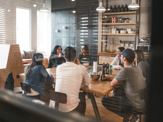 Group of people seated around a wooden table in a modern cafe, chatting and sharing drinks in a casual meeting.