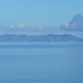 Calm blue sea with a distant mountainous island on the horizon under a pale cloud-filled sky.