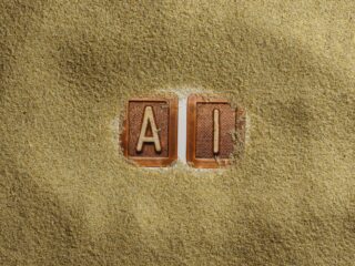 Two clay letter tiles, A and I, partially buried in golden sand on a beach surfacecreme.